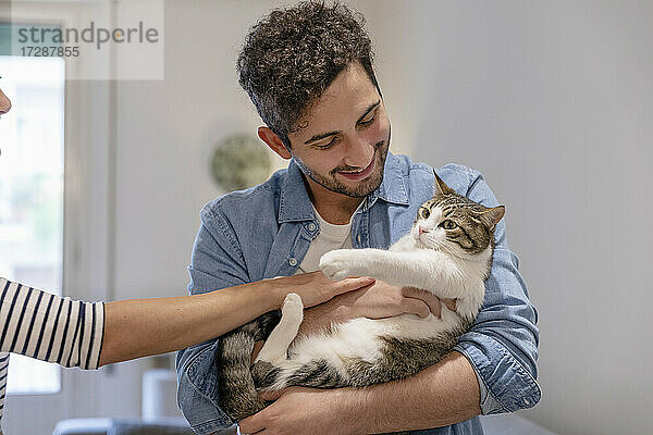 Lächelnder Mann spielt mit getigerter Katze zu Hause