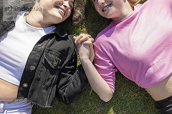 Glückliche Freundinnen  die sich an den Händen halten und auf dem Gras in einem öffentlichen Park liegen