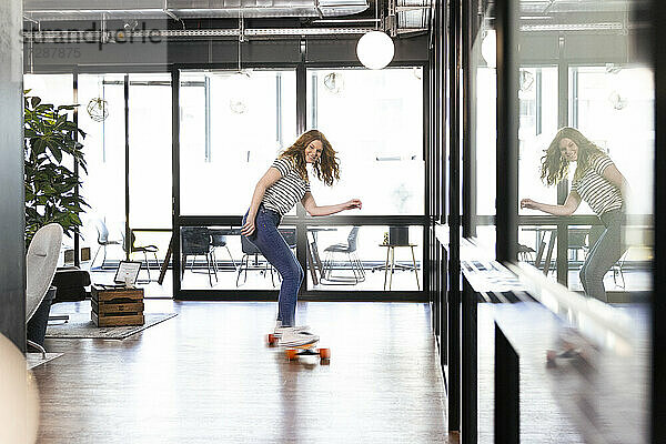 Lächelnde kreative Geschäftsfrau auf dem Skateboard im Büro