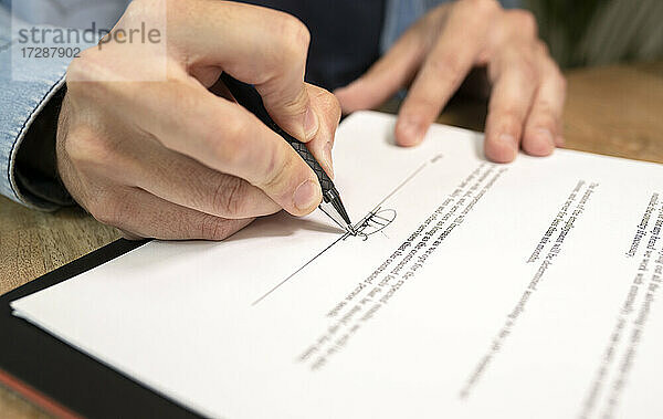 Männlicher Fachmann bei der Unterschrift auf einem Dokument im Büro