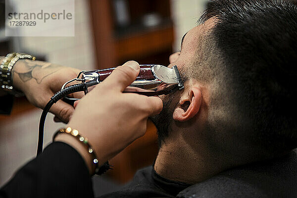 Männlicher Friseur  der einem Mann mit einem elektrischen Rasiermesser die Haare schneidet