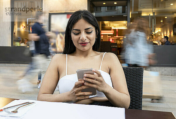 Junge Frau benutzt ihr Smartphone  während sie in einem Café am Tisch sitzt