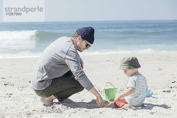Mann und Sohn spielen mit Sandspielzeug am Wasser am Strand