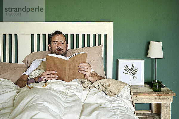 Mittlerer erwachsener Mann liest ein Buch und ruht sich im Schlafzimmer aus
