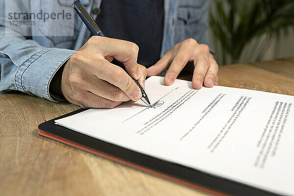 Geschäftsmann macht Unterschrift auf Vertrag am Schreibtisch im Büro