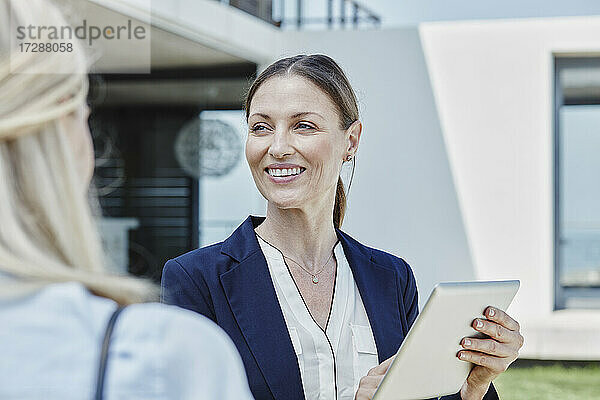 Lächelnde Immobilienmaklerin mit digitalem Tablet in der Hand eines Kunden