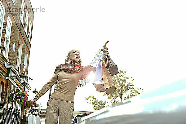 Lächelnde Frau mit Einkaufstüten  die in der Stadt ein Taxi ruft