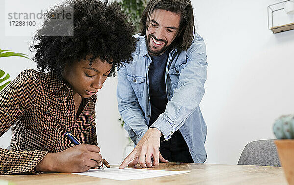 Lächelnder Geschäftsmann  der eine Kollegin bei der Unterzeichnung eines Dokuments an einem Schreibtisch im Büro begleitet