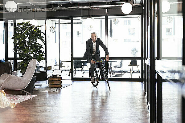Lächelnder Geschäftsmann beim Radfahren im Büro