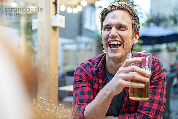 Mann lacht  während er in einer Kneipe ein Bierglas hält