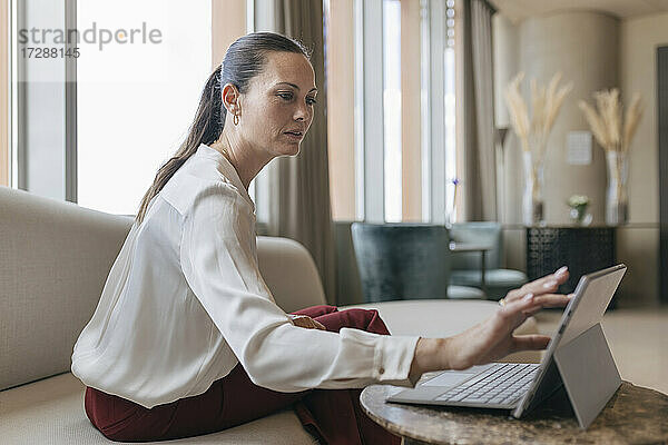 Weibliche Fachkraft  die ein digitales Tablet benutzt  während sie auf dem Sofa im Büro sitzt