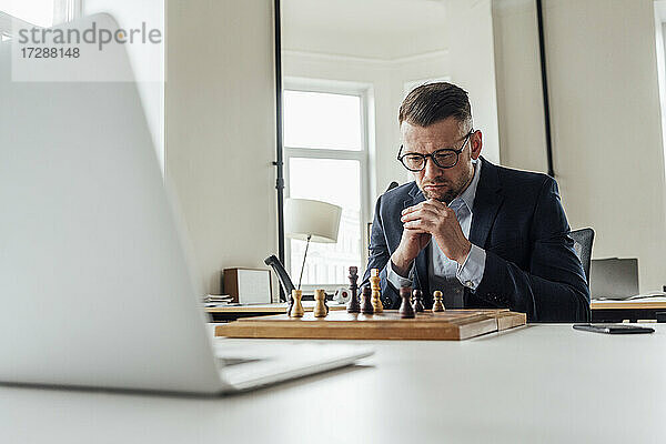 Männlicher Unternehmer mit Hand am Kinn spielt Schach im Büro