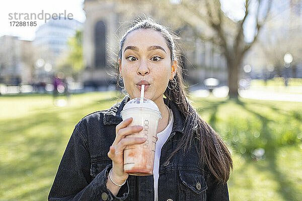 Junge Frau mit schielendem Blick beim Trinken eines Milchshakes im Park