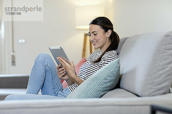 Lächelnde Frau mit digitalem Tablet auf dem Sofa im Wohnzimmer