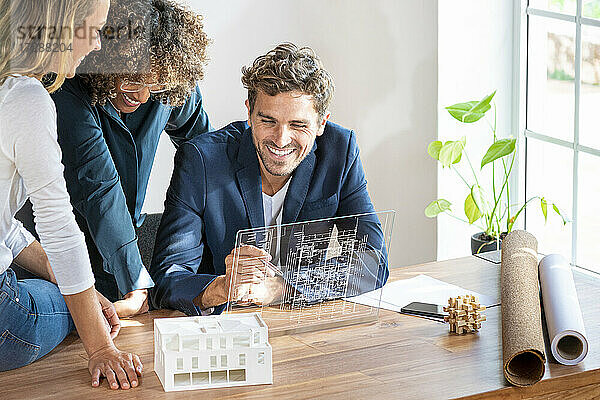 Männlicher Architekt mit futuristischem Bildschirm bei der Arbeit mit Kollegen im Büro