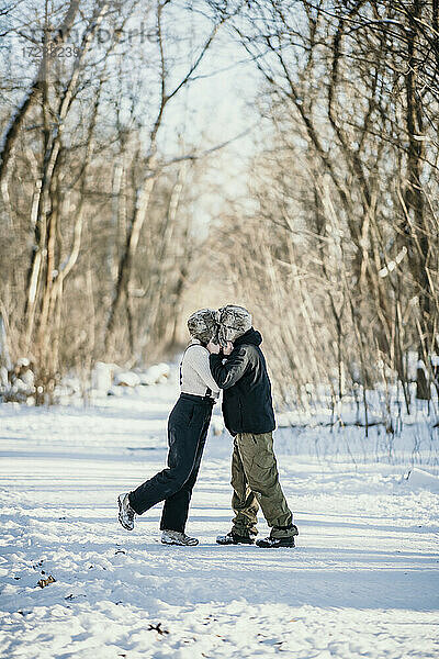 Mid adult couple kissing each other while standing on snow path in forest