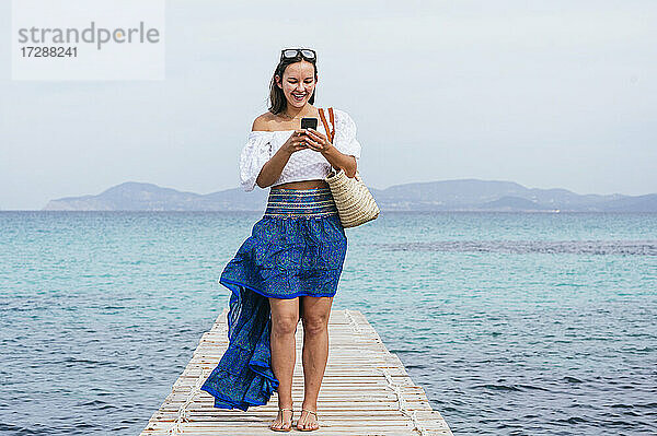 Lächelnde Frau  die ein Smartphone benutzt  während sie auf einem Steg steht