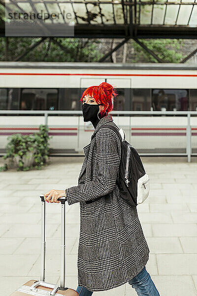 Rothaarige Frau mit Gesichtsschutzmaske beim Spaziergang am Bahnhof