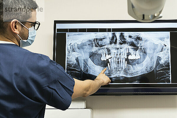 Männlicher Zahnarzt mit Gesichtsschutzmaske bei der Untersuchung eines Röntgenbildes in einer Klinik