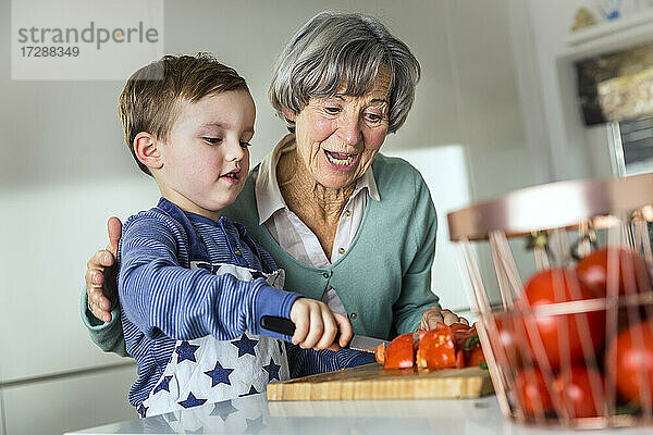Enkel schneidet Tomate bei Großmutter in der Küche