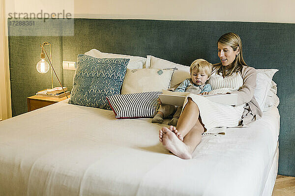 Schwangere Frau im Gespräch mit ihrem Sohn  während sie ein Fotoalbum auf dem Bett zu Hause zeigt