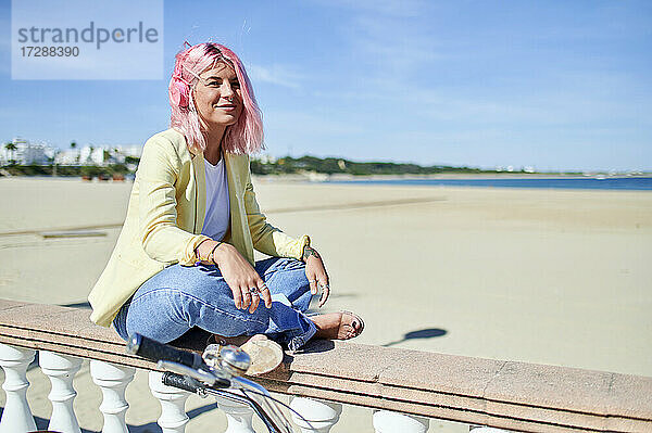 Lächelnde Frau auf der Promenade am Strand sitzend