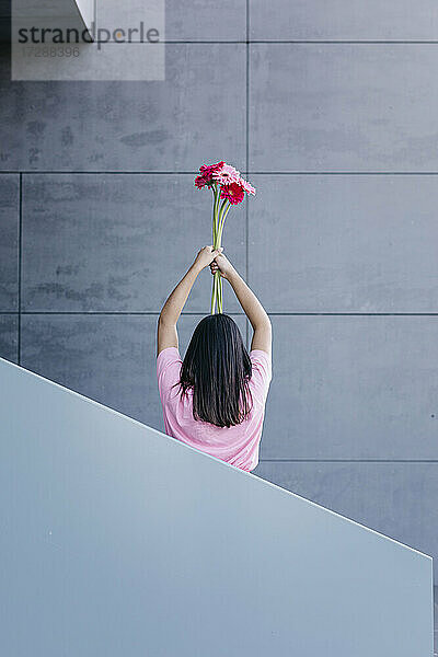 Junge Frau hält einen Blumenstrauß vor einer grauen Wand