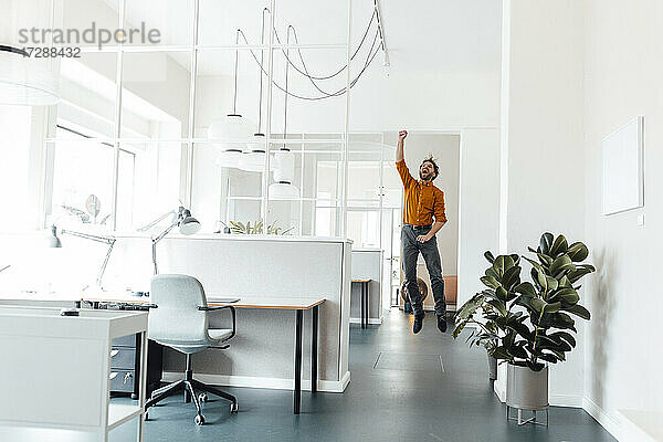 Männlicher Unternehmer jubelt beim Springen im Büro
