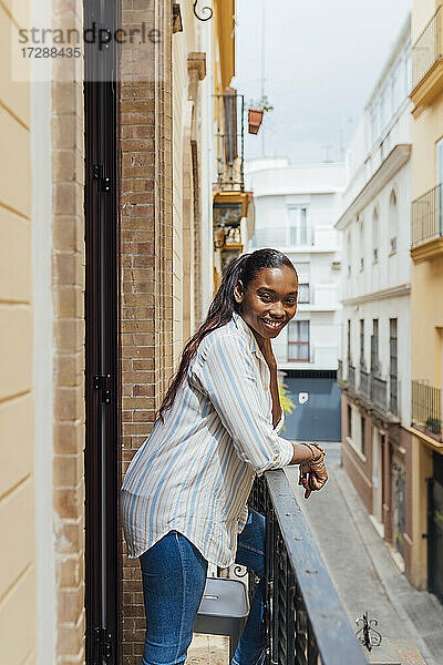 Lächelnde Frau  die sich auf einem Balkon an ein Geländer lehnt