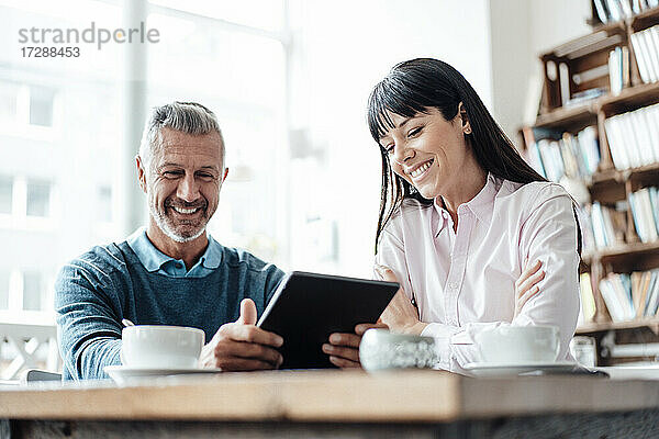 Lächelnder Geschäftsmann  der ein digitales Tablet von einem Kollegen in einem Café benutzt