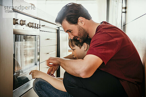 Vater mit Sohn schaut bei der Zubereitung von Speisen in den Ofen