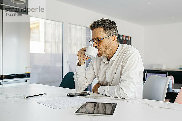 Geschäftsmann trinkt Kaffee  während er an der Kücheninsel im Heimbüro sitzt