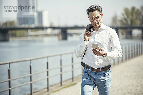 Reifer männlicher Unternehmer  der an einem sonnigen Tag ein Mobiltelefon benutzt