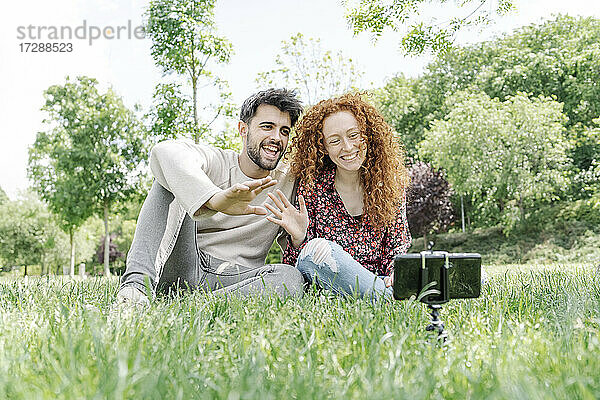 Glückliches junges Paar winkt beim Vlogging im öffentlichen Park