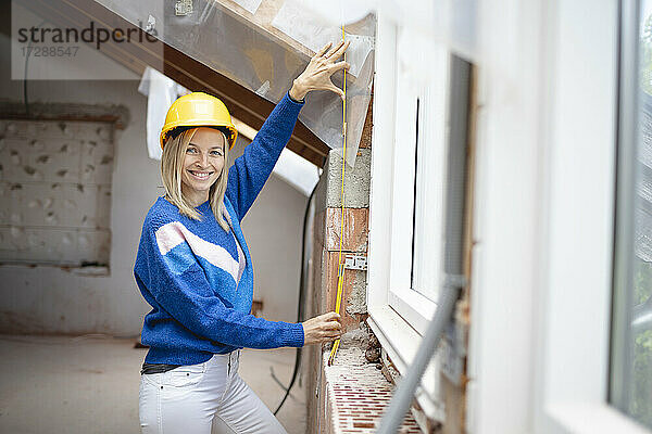 Lächelnde Bauunternehmerin  die auf der Baustelle mit einem Zollstock misst