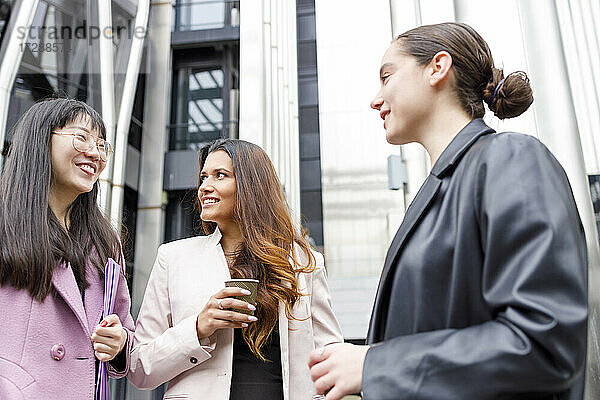 Unternehmerinnen mit Kaffeetasse und Aktenordner im Gespräch  während sie zusammen stehen