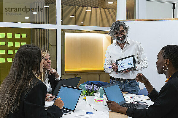 Männliche und weibliche Unternehmer betrachten eine Geschäftsfrau  die während eines Treffens in einem Konferenzraum im Büro diskutiert