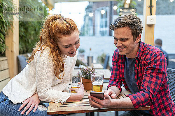 Paar schaut auf sein Smartphone  während es in einer Kneipe Bier trinkt