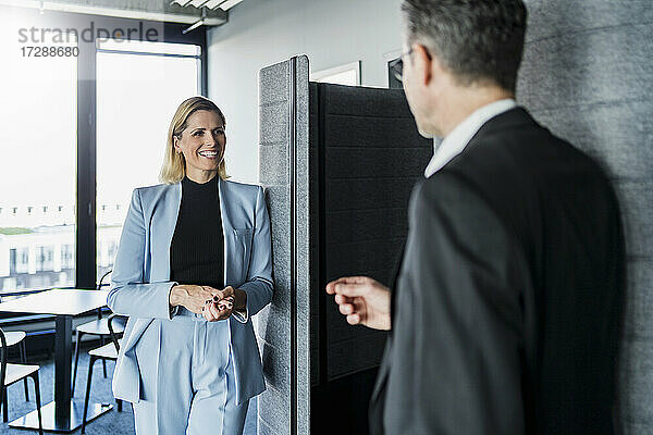 Lächelnde Geschäftsfrau  die einen männlichen Kollegen anschaut  während sie im Büro diskutiert