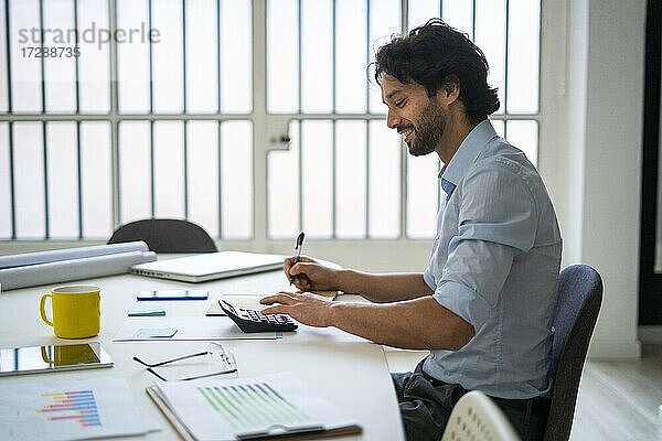 Lächelnder junger Geschäftsmann  der am Schreibtisch im Büro sitzt und arbeitet