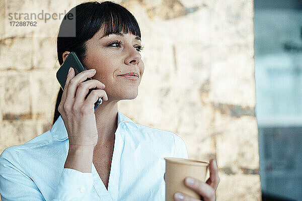 Unternehmerin hält Kaffeetasse und spricht mit dem Handy