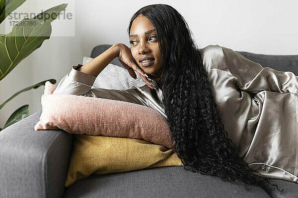 Frau mit langen schwarzen Haaren liegt auf dem Sofa und träumt zu Hause vor sich hin