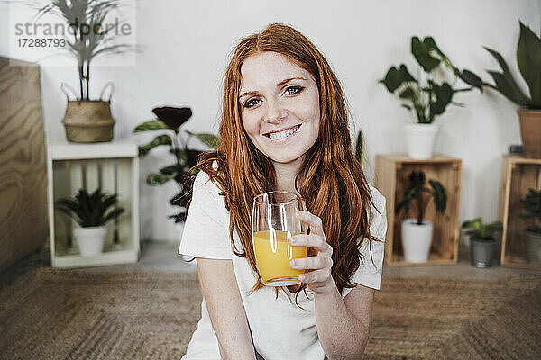 Lächelnde schöne Frau hält ein Glas Saft zu Hause