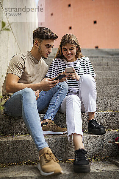 Paar benutzt Mobiltelefon  während es auf einer Treppe sitzt