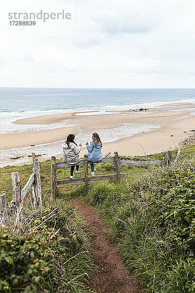 Freundinnen sitzen auf einem Holzzaun am Strand