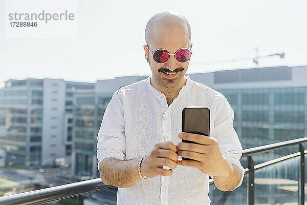 Lächelnder Mann  der ein Smartphone benutzt  während er auf einem Balkon steht