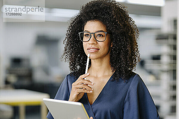 Nachdenkliche Geschäftsfrau mit digitalem Tablet und digitalisiertem Stift im Büro stehend