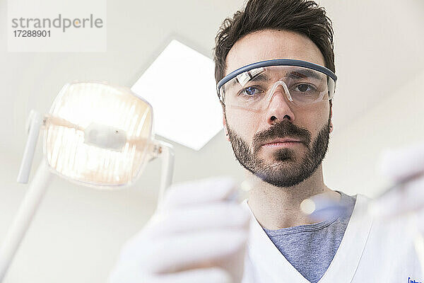 Männlicher Zahnarzt mit Schutzbrille bei der Arbeit in einer medizinischen Klinik