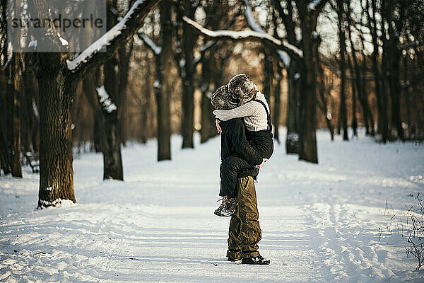 Freund trägt seine Freundin im Schnee stehend im Wald