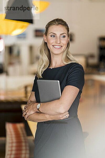 Lächelnde schöne Unternehmerin  die im Büro ein digitales Tablet hält und dabei wegschaut